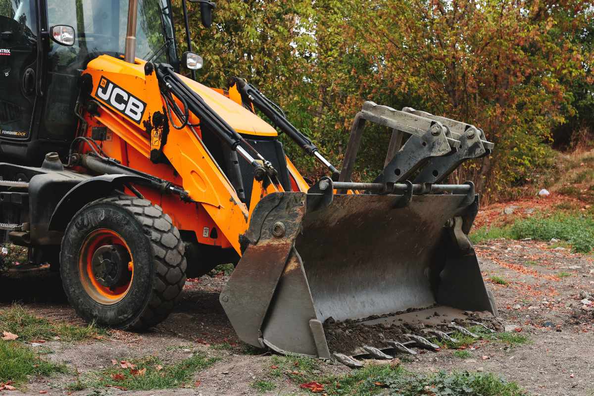 Mann bedient einen roten Minibagger und bewegt Erde auf einer Gartenfläche.
