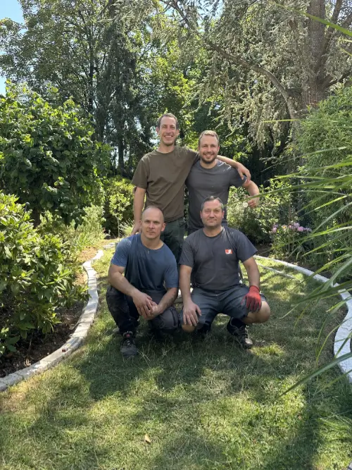 Vier Gärtner stehen gemeinsam in einer gepflegten Gartenanlage und lächeln in die Kamera.